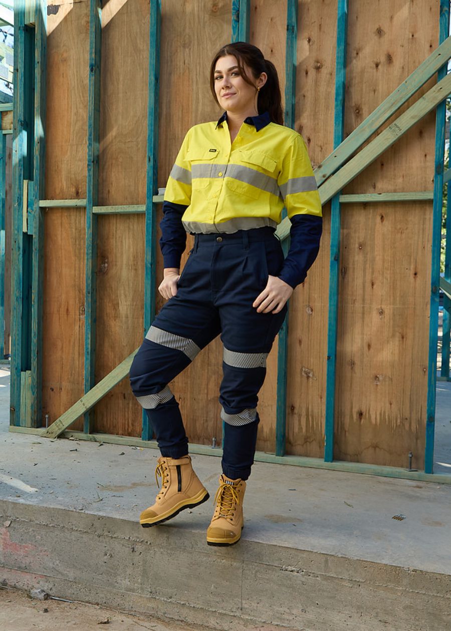 Woman on work site wearing fluorescent yellow and navy long sleeve top that features two reflective stripes.