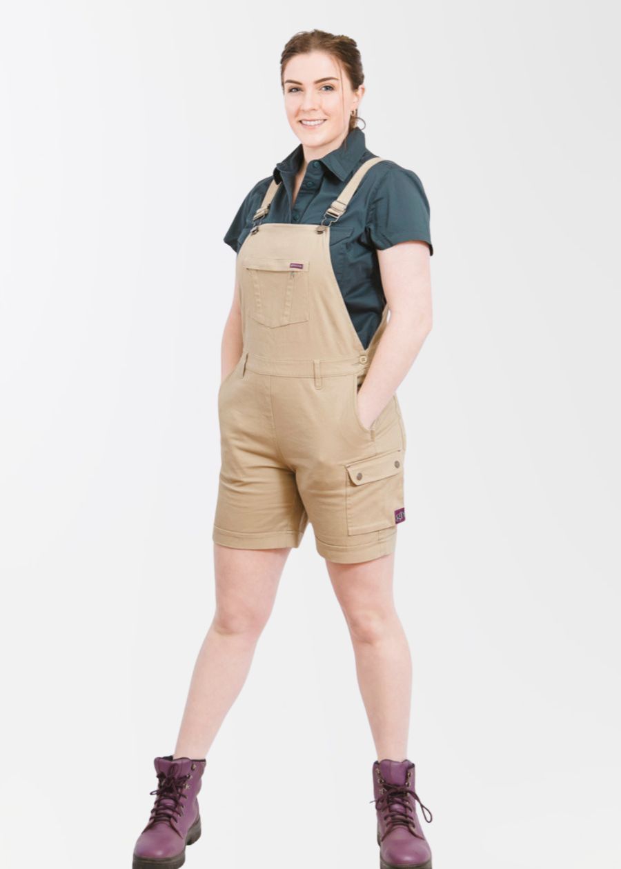 Woman wearing short overalls in light brown colour with hands in pockets.