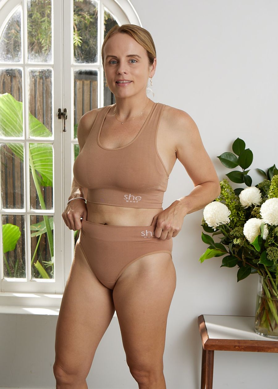 front view of woman standing in front of window with neutral coloured bamboo racer bra and full briefs