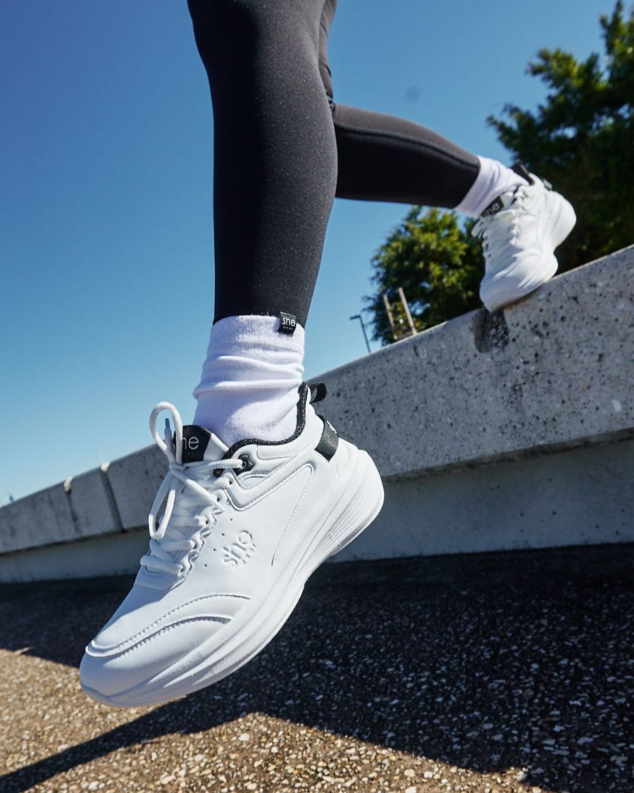 Woman taking a step off a ledge wearing white walking sneaker
