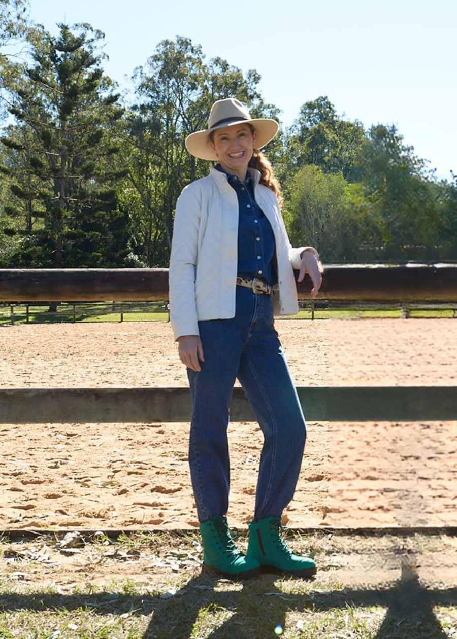 Woman standing out front of a paddock wearing green Achieves zip-up safety boot. 
