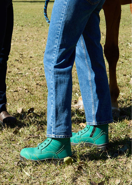 Person wearing green lace-up safety boots in grass. 