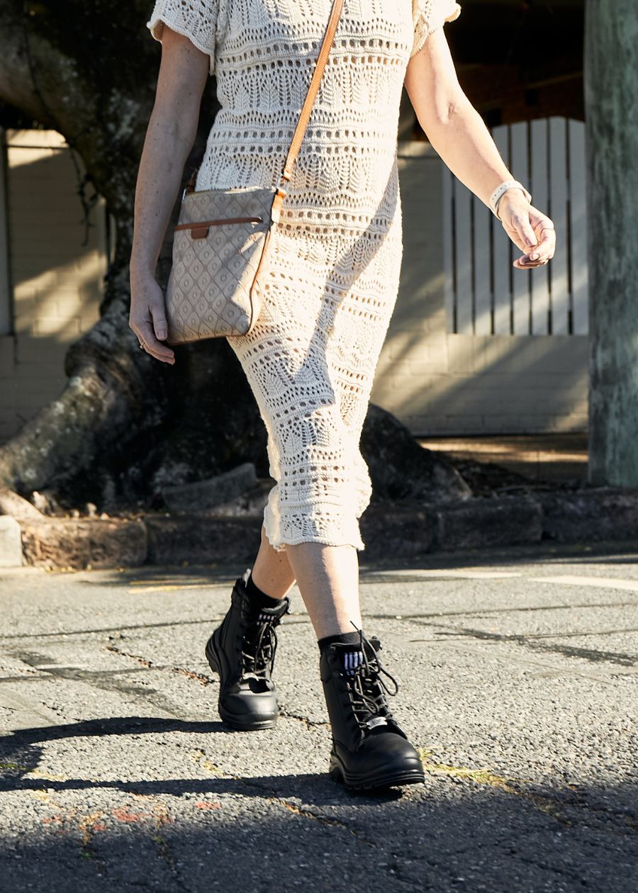 woman crossing street in cream dress and black fashion boots 