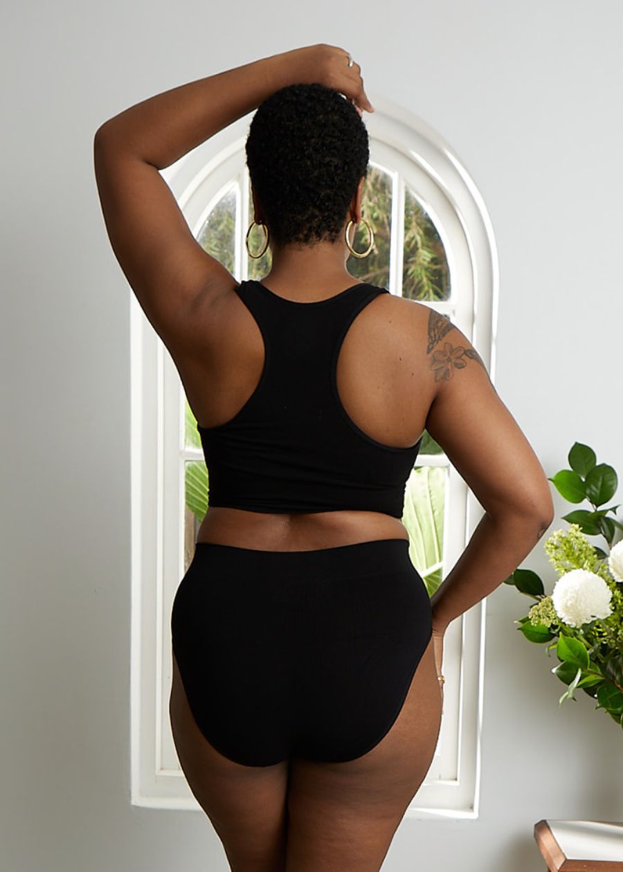 Rear view of woman wearing a soft-cup black racerback crop top bra and high-cut briefs made of stretchy organic bamboo. 