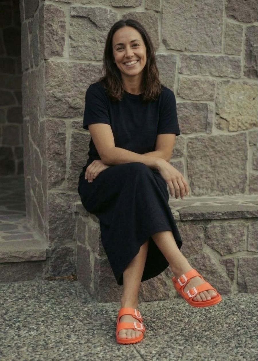 Woman sitting on concreate slab wearing bright orange slides. 