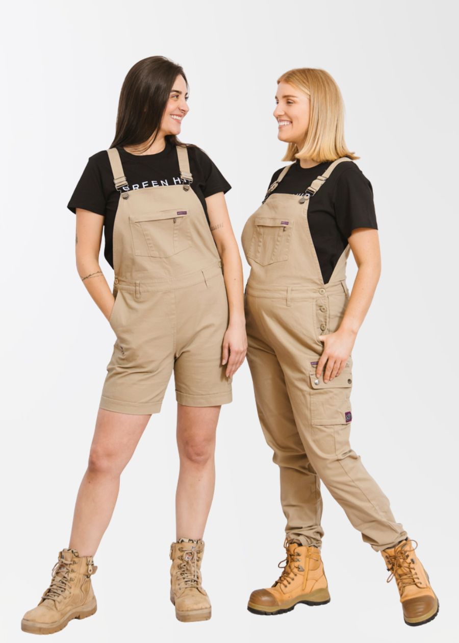 Woman on left wearing short khaki overalls with hand in pocket. Woman on left wearing long khaki overalls. 