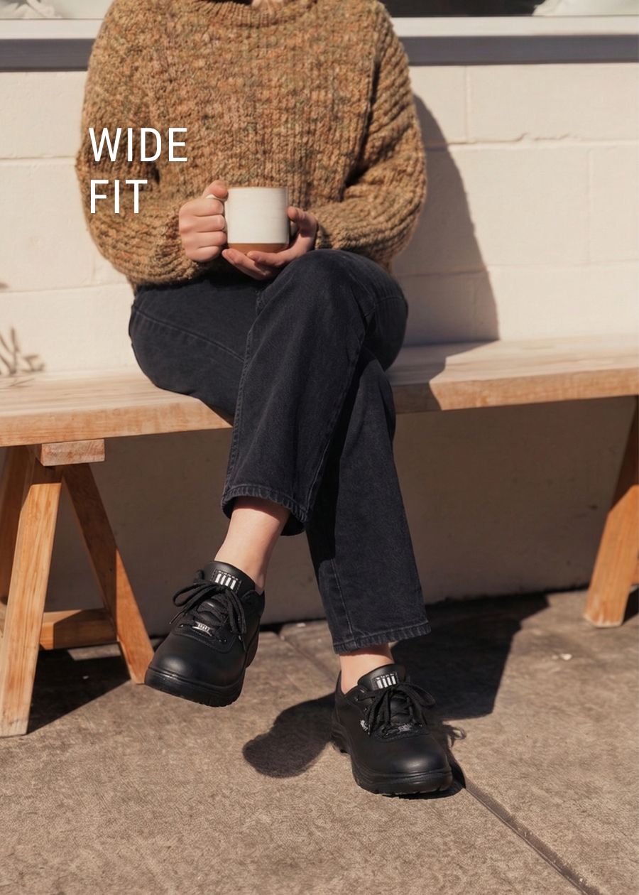 Lady sat down with a mug wearing wide fit black working shoe