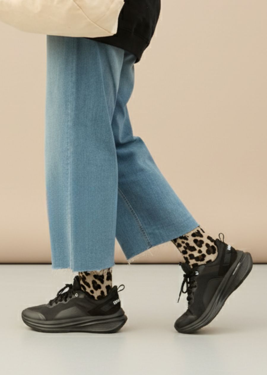 Side view of person wearing leopard print socks an black lace-up walking shoes. 