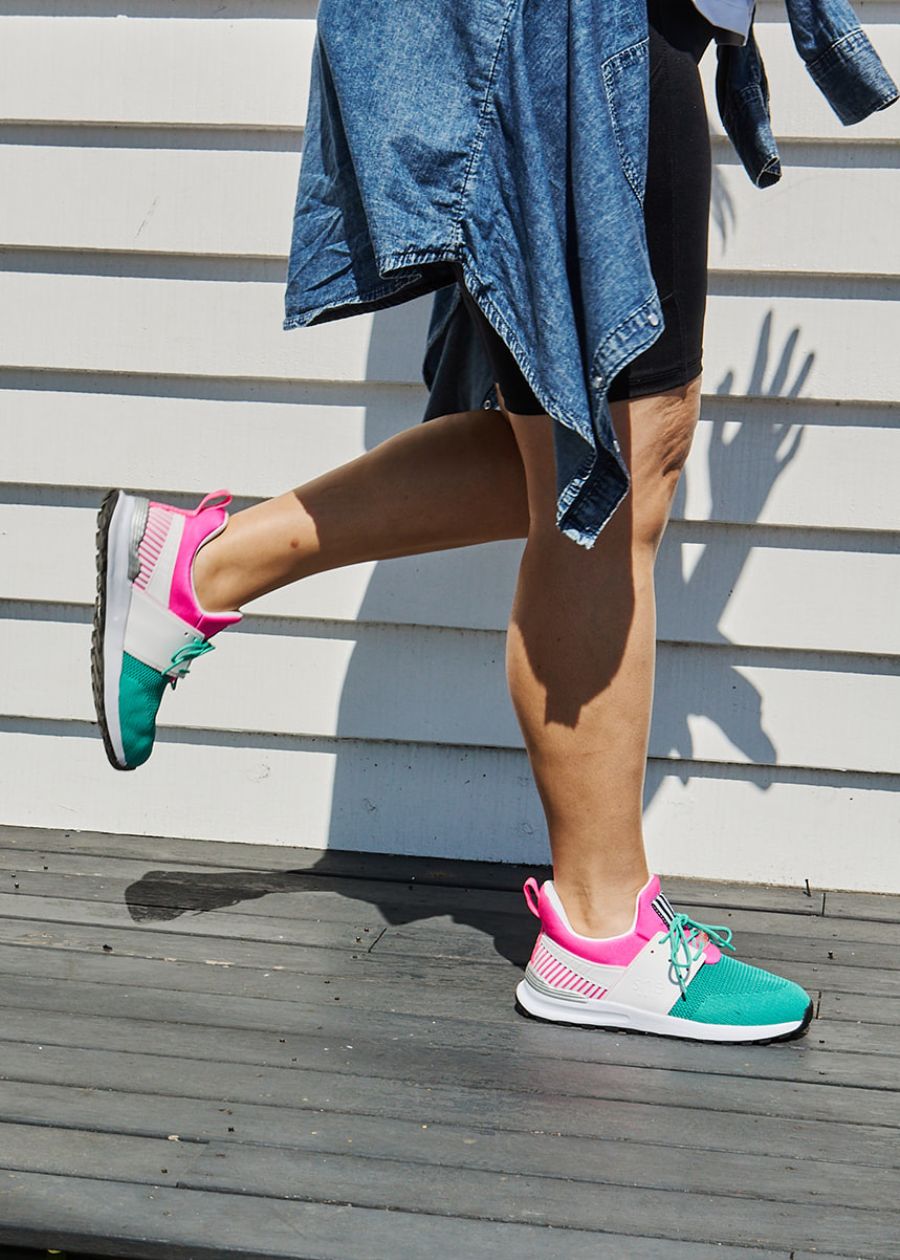 Side view of women wearing bright pink, green, and white active sneakers. 
