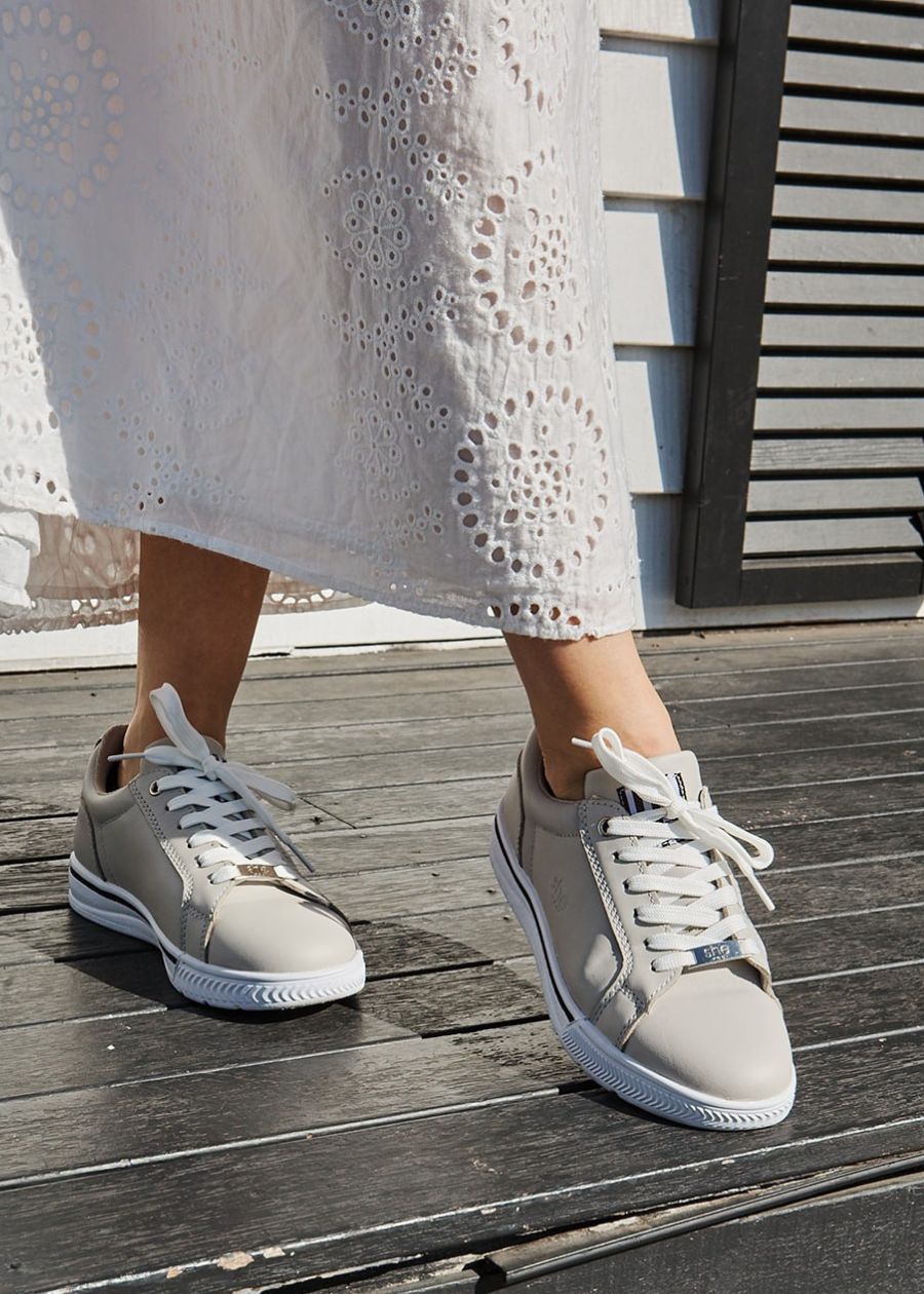 Women feet, toe pointed. Wearing beige sneakers with white laces, and white sole. 