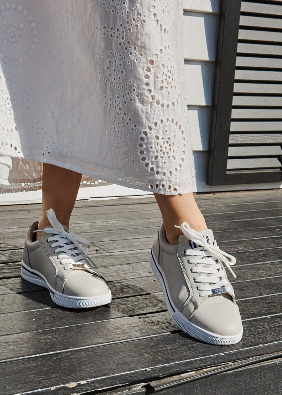 Women feet, toe pointed. Wearing beige sneakers with white laces, and white sole. 