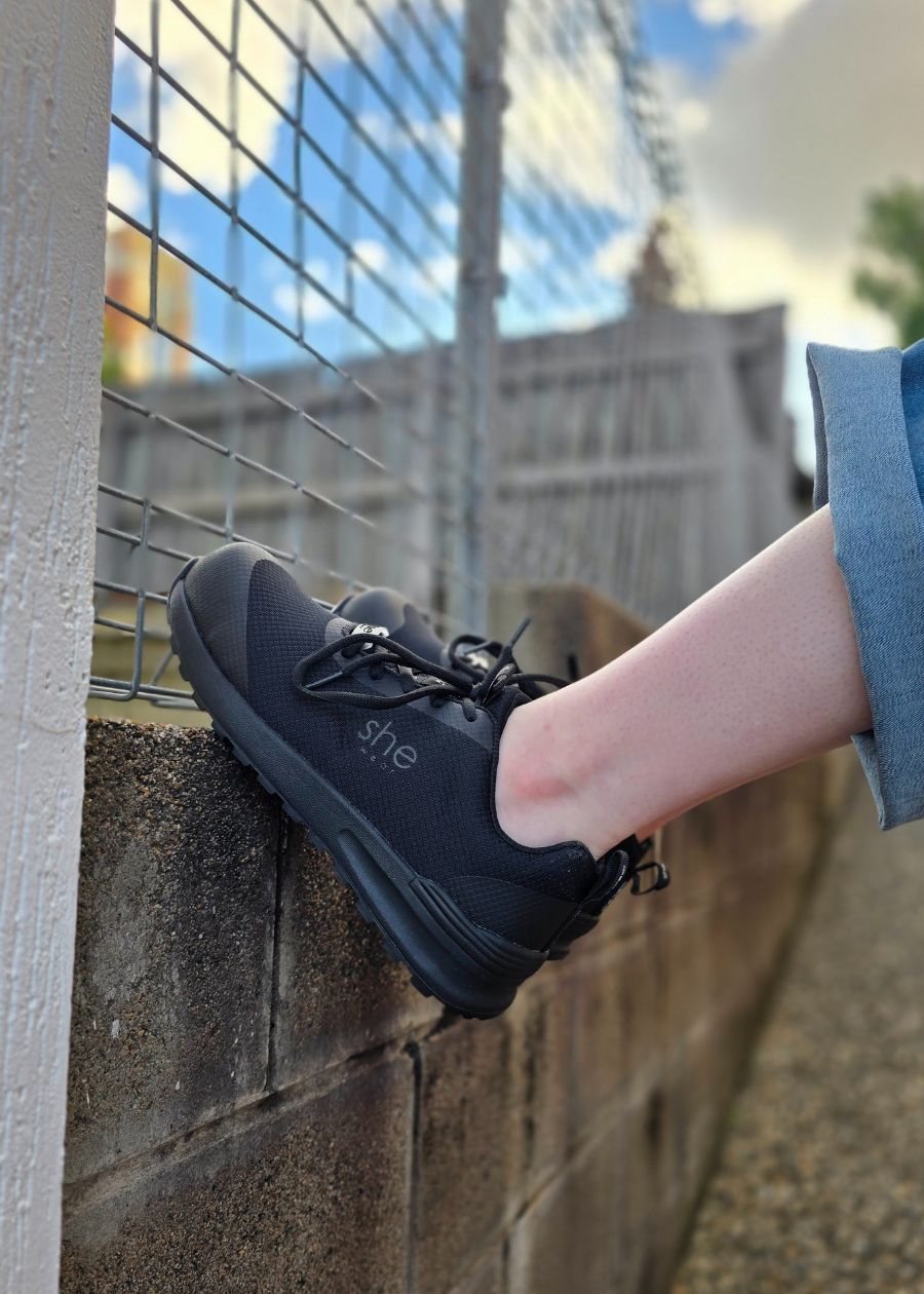 Feet braced against a stone wall, wearing black safety sneakers